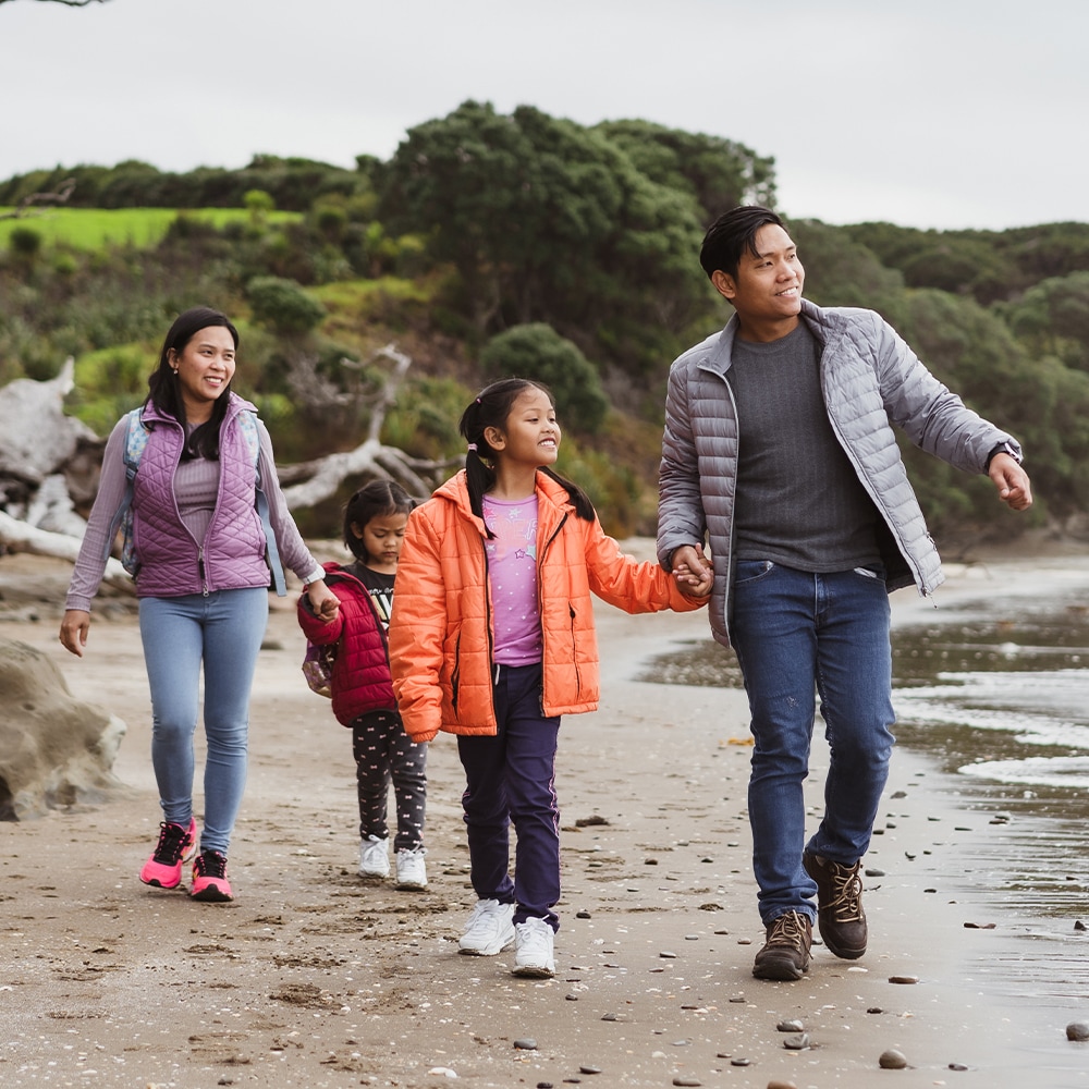 An asian family are strolling along the beach holding hands